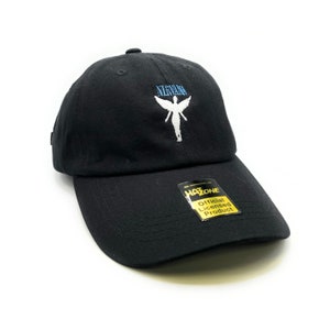 May include: Black baseball cap with a white angel graphic and the word "Nirvana" embroidered in blue on the front. The cap has a yellow tag that says "Official Licensed Product" and "HAZ-ZONE".
