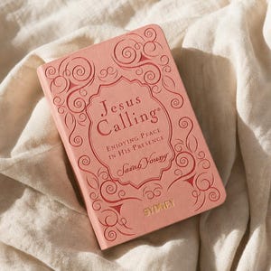 May include: A coral-colored book titled Jesus Calling: Enjoying Peace in His Presence by Sarah Young, featuring an embossed scrollwork border and the name SYDNEY printed in gold lettering at the bottom of the front cover.
