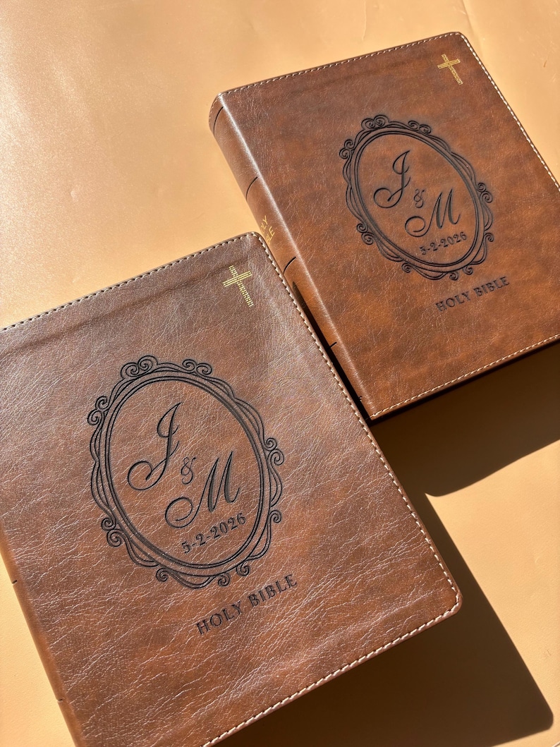 May include: Two brown leather Holy Bibles with gold crosses and decorative oval designs. The oval design contains the initials "J & M" and the date "5-2-2026". The words "Holy Bible" are printed at the bottom of the cover.