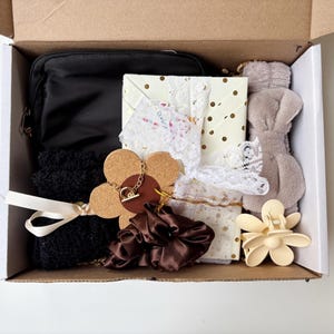 May include: A gift box containing a black cosmetic bag, wrapped presents with lace and polka dots, a brown scrunchie, a flower-shaped hair clip, black socks tied with a cream ribbon, and a plush bunny ear headband.