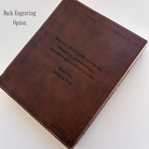 May include: A brown leather-bound book with stitched edges. The cover features engraved text: "May this Word guide your home, strengthen your marriage, and bless generations to come. With love, Mom & Dad."