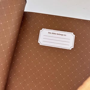 May include: Open Bible with brown pages featuring a diamond pattern with small white dots. A white label with the text "This Bible belongs to:" is visible. The binding is a darker brown.