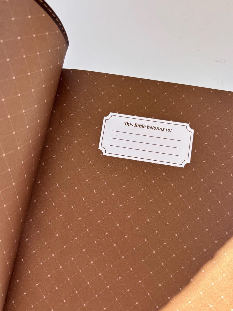 May include: Open Bible with brown pages featuring a diamond pattern with small white dots. A white label with the text "This Bible belongs to:" is visible. The binding is a darker brown.