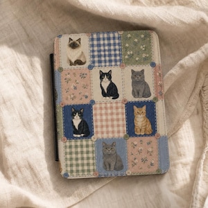 Puede incluir: Una funda rectangular para lector electrónico con un diseño de patchwork que muestra ilustraciones de gatos, patrones florales y cuadros vichy. La cuadrícula está decorada con pequeños botones de colores en las intersecciones.