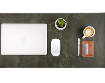 May include: An overhead shot of a green leather desk mat with a laptop, mouse, pen, wallet, small plant, and a cup of coffee with latte art. The desk mat is rectangular and has a distressed finish.