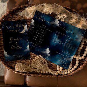 Puede incluir: Un programa de boda con fondo azul oscuro y letras doradas. El programa presenta una luna creciente y estrellas. El texto del programa dice "Bienvenido a la boda de Jennifer y Phillip".