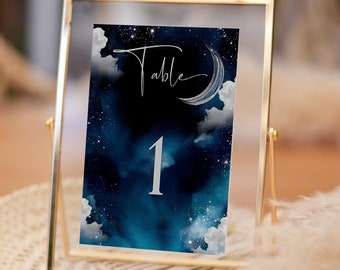 May include: A gold-framed table number sign with a blue and white watercolor background featuring clouds, stars, and a crescent moon. The number "1" is written in silver and the text "Table" is written in cursive. The sign is 5x7 inches.