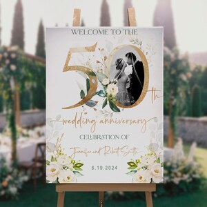 Pode incluir: Um cartaz de boas-vindas de 46x61 cm para uma celebração de 50º aniversário de casamento. O cartaz apresenta um 50 dourado com flores brancas e vegetação, uma foto em preto e branco do casal e o texto "Bem-vindos ao 50º aniversário de casamento de Jennifer e Robert Smith 6.19.2024".