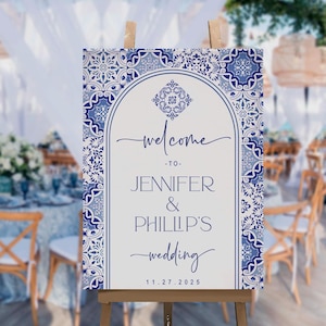 Puede incluir: Un cartel de bienvenida blanco con un borde estampado en azul y blanco. El cartel dice "Bienvenido a Jennifer & Phillip's Wedding 11.27.2025".