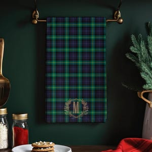 May include: A rectangular hand towel featuring a green, blue, and black plaid pattern with a gold letter M monogram inside a circular wreath. The towel measures 28 by 16 inches and is made of 52 percent polyester and 48 percent cotton.