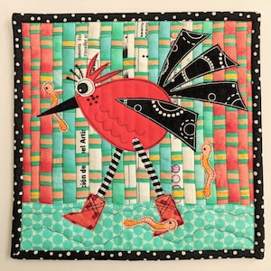 Könnte beinhalten: Eine rote und schwarze Vogel-Applikation auf einem gestreiften Hintergrund. Der Vogel hat einen langen Schnabel und große Augen. Der Hintergrund ist ein Patchwork aus bunten Streifen. Der Vogel geht auf einer blauen und grünen Oberfläche mit einem weißen Punktmuster.