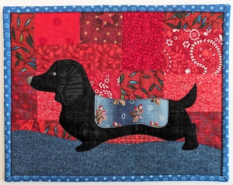 Könnte beinhalten: Eine schwarze Dackel-Applikation auf einem roten und blauen Patchwork-Decken. Die Decke besteht aus verschiedenen Stoffen, darunter Denim, Paisley und Blumenmuster.
