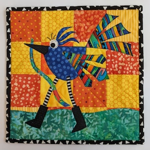 Könnte beinhalten: Eine bunte Patchwork-Decke mit einem blauen Vogel mit schwarz-weißen Streifen und einem langen gelben Schwanz. Der Vogel ist umgeben von Quadraten aus gelbem, orangem und rotem Stoff mit geometrischen Mustern.