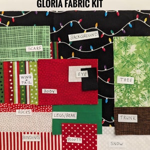 May include: A fabric kit labeled "GLORIA FABRIC KIT" with various fabric pieces. Includes green, red, and white patterned fabrics for a scarf, body, wing/tail, rocks, binding, boots, tree, trunk, and background. The background fabric is black with string lights.