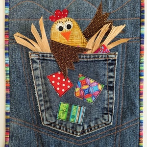 Könnte beinhalten: Eine Jeans-Patchwork-Decke mit einer braunen und gelben Hühner-Applikation in einer Tasche. Die Tasche enthält auch bunte Stoffreste.