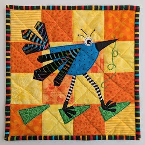 Könnte beinhalten: Eine bunte Patchwork-Decke mit einem skurrilen blauen Vogel mit schwarzen und weißen Streifen, einem großen Auge und einem langen, grünen Schwanz. Der Vogel steht auf grünen und orangen Quadraten mit gelbem Hintergrund.