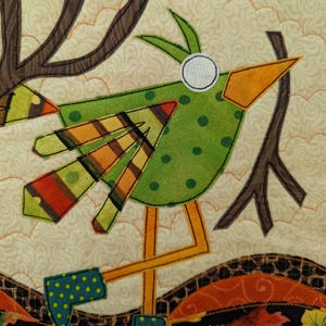 K&ouml;nnte beinhalten: Ein skurriler, gesteppter Vogel mit gr&uuml;nem, gepunktetem K&ouml;rper, orangefarbenem Schnabel und gestreiften Fl&uuml;geln. Der Vogel steht auf gelben Beinen und tr&auml;gt blaue, gepunktete Stiefel. Der Hintergrund zeigt einen Baum und Herbstbl&auml;tter.