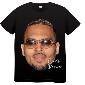 Op de afbeelding: Zwart T-shirt met een foto van Chris Brown die een zonnebril draagt. De tekst "Chris Brown" is in wit onder de foto gedrukt.