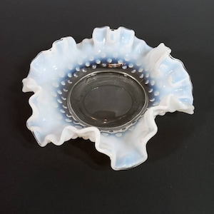May include: A vintage, opalescent glass bowl with a ruffled edge. The bowl has a clear, circular center and a rim dotted with small, raised beads. The outer edge is a wavy, ruffled design, creating a delicate, antique aesthetic.