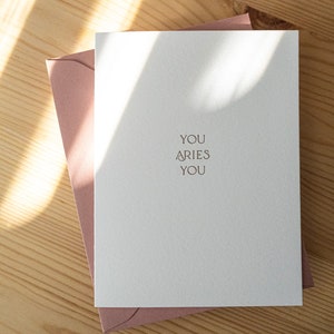 Aries zodiac birthday card letterpress printed in matte gold ink onto bright white cotton paper with a pink envelope