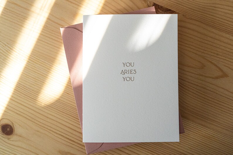 Aries zodiac birthday card letterpress printed in matte gold ink onto bright white cotton paper with a pink envelope