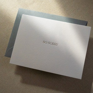 Sympathy card letterpress printed with So Sorry in matte gold ink onto bright white cotton paper with a blue envelope