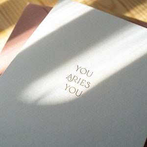 Aries zodiac birthday card letterpress printed in matte gold ink onto bright white cotton paper with a pink envelope