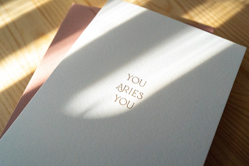 Aries zodiac birthday card letterpress printed in matte gold ink onto bright white cotton paper with a pink envelope