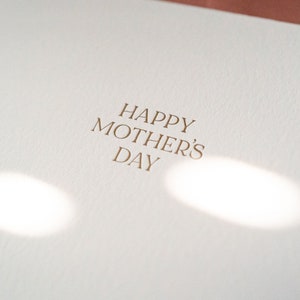 Peut inclure: Une carte blanche avec le texte "Happy Mother's Day" imprim&eacute; en lettres dor&eacute;es.