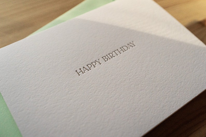 Happy birthday card letterpress printed in matte gold ink onto bright white cotton paper with a light green envelope