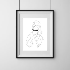 May include: Line art print of a person wearing a towel on their head and sunglasses, holding a cup in one hand.