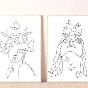 May include: Two black and white line art prints of a woman's face with butterflies around her head. The woman in the left print has her eyes closed, while the woman in the right print has her eyes open and is looking up.