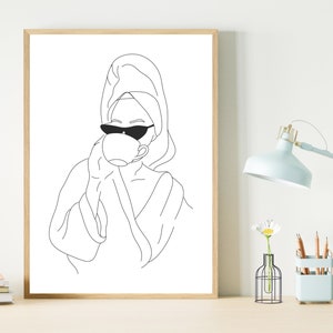 May include: Line art drawing of a person wearing a towel on their head and sunglasses, drinking from a cup. The drawing is in black and white and is framed in a wooden frame.