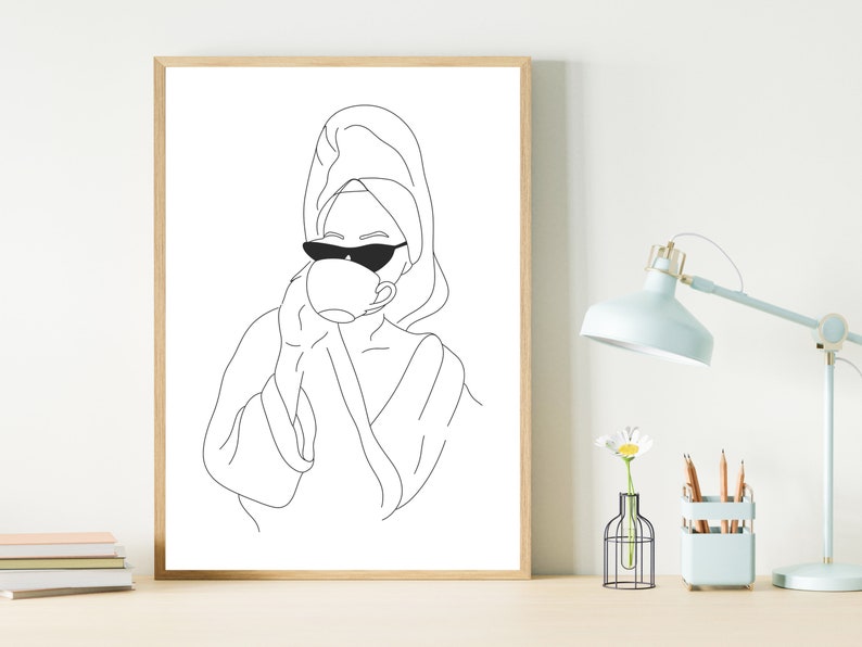 May include: Line art drawing of a person wearing a towel on their head and sunglasses, drinking from a cup. The drawing is in black and white and is framed in a wooden frame.