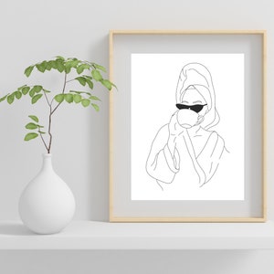 May include: Line art drawing of a person wearing a bathrobe and sunglasses, holding a cup of coffee or tea. The drawing is in black and white and is framed in a light wood frame.