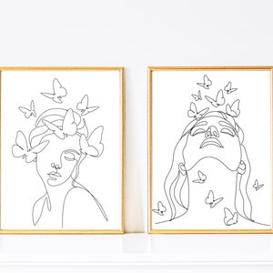 May include: Two black and white line art prints of women's faces with butterflies surrounding them. The prints are framed in gold.