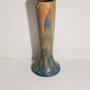 May include: A small, blue and brown ceramic vase with a flared base. The vase has a unique, abstract design.