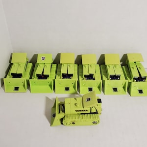May include: A set of seven lime green toy construction vehicles, including a bulldozer. The vehicles are all in the same style, with a raised cab and a large scoop in the front. The bulldozer has a black cab and a black scoop.