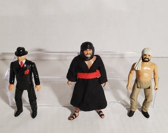 May include: Three action figures, one in a black suit and fedora, one in a black robe with a red sash, and one in tan pants and a white head wrap.