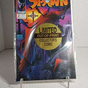 Pode incluir: Uma banda desenhada com Spawn, um personagem de super-herói vermelho e preto, com um autocolante dourado que diz "Limited Out-of-Print Collector's Comic".