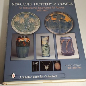 May include: Book cover featuring a blue background with the title "Newcomb Pottery & Crafts: An Educational Enterprise for Women 1895-1940". The cover also features images of pottery, including a plate with a pine tree design, a vase with a floral design, and a tall vase with a tree design.