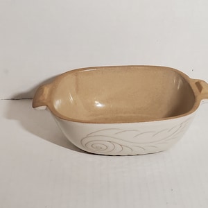 以下が含まれることがあります： 茶色の釉薬と渦巻き模様が施された白いセラミック製のベーキングディッシュ。ディッシュには両側に2つのハンドルが付いています。