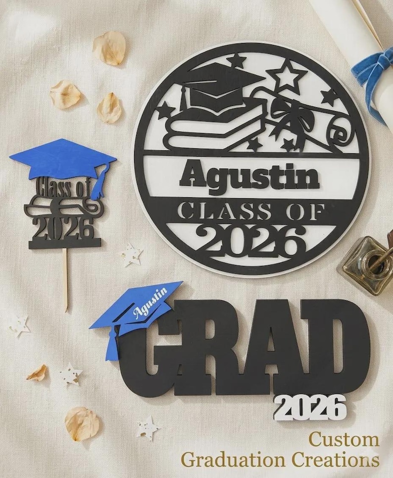 K&ouml;nnte beinhalten: Abschlussdekorationen, darunter ein gro&szlig;es schwarz-wei&szlig;es rundes Schild mit dem Namen "Agustin" und "Klasse von 2026". Au&szlig;erdem ein blau-schwarzes "Grad"-Schild mit "2026" und eine blaue Abschlusskappe.