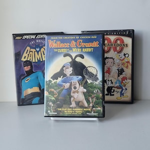 May include: Three DVD cases featuring animated movies. The titles include "Batman: The Movie," "Wallace & Gromit: The Curse of the Were-Rabbit," and "90s Cartoons." The cases are black with colorful artwork.