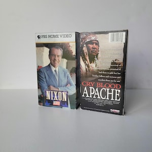 May include: Two VHS tapes. One features Richard Nixon with the text "NIXON" and "PBS HOME VIDEO". The other tape is titled "CRY BLOOD APACHE" with an image of a Native American man.