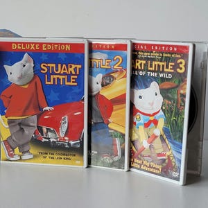 May include: Three DVD cases for the "Stuart Little" movie series. The first case is labeled "Deluxe Edition" and features Stuart Little in front of a red car. The second case is "Stuart Little 2", and the third is "Stuart Little 3: Call of the Wild".