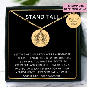 May include: Gold necklace with a round pendant featuring a detailed illustration of Medusa. The pendant is in a black box with the words "Stand Tall" and a message about strength and bravery. The back of the necklace can be personalized with an engraved message.