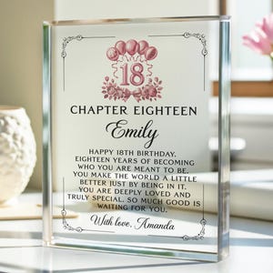 May include: A clear acrylic block with the text "Chapter Eighteen" and "Emily" in elegant script. The design includes pink balloons, floral accents, and a message for an 18th birthday. The text reads "Happy 18th Birthday..." and is signed "With love, Amanda."