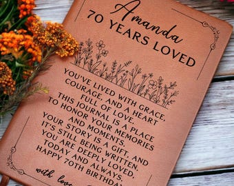 May include: A brown leather journal with the text "Amanda 70 Years Loved" and a message about living with grace, courage, and a heart full of love. The journal is a place to honor memories and moments. The message ends with "Happy 70th Birthday" and "with love, Emily".