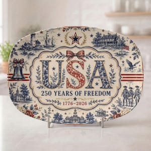 May include: An oval ceramic platter featuring a blue and red patriotic design with the text USA 250 YEARS OF FREEDOM 1776-2026. The illustration includes a lighthouse, a ship, a colonial building, a bell, an eagle, and soldiers in uniform.